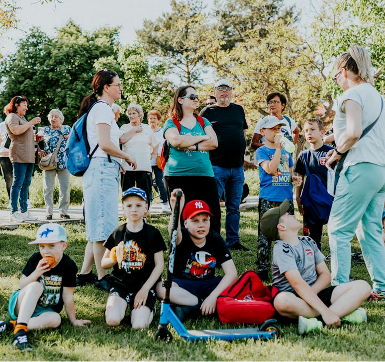 A diverse group of families and children enjoying an outdoor event on a sunny day in a park setting.