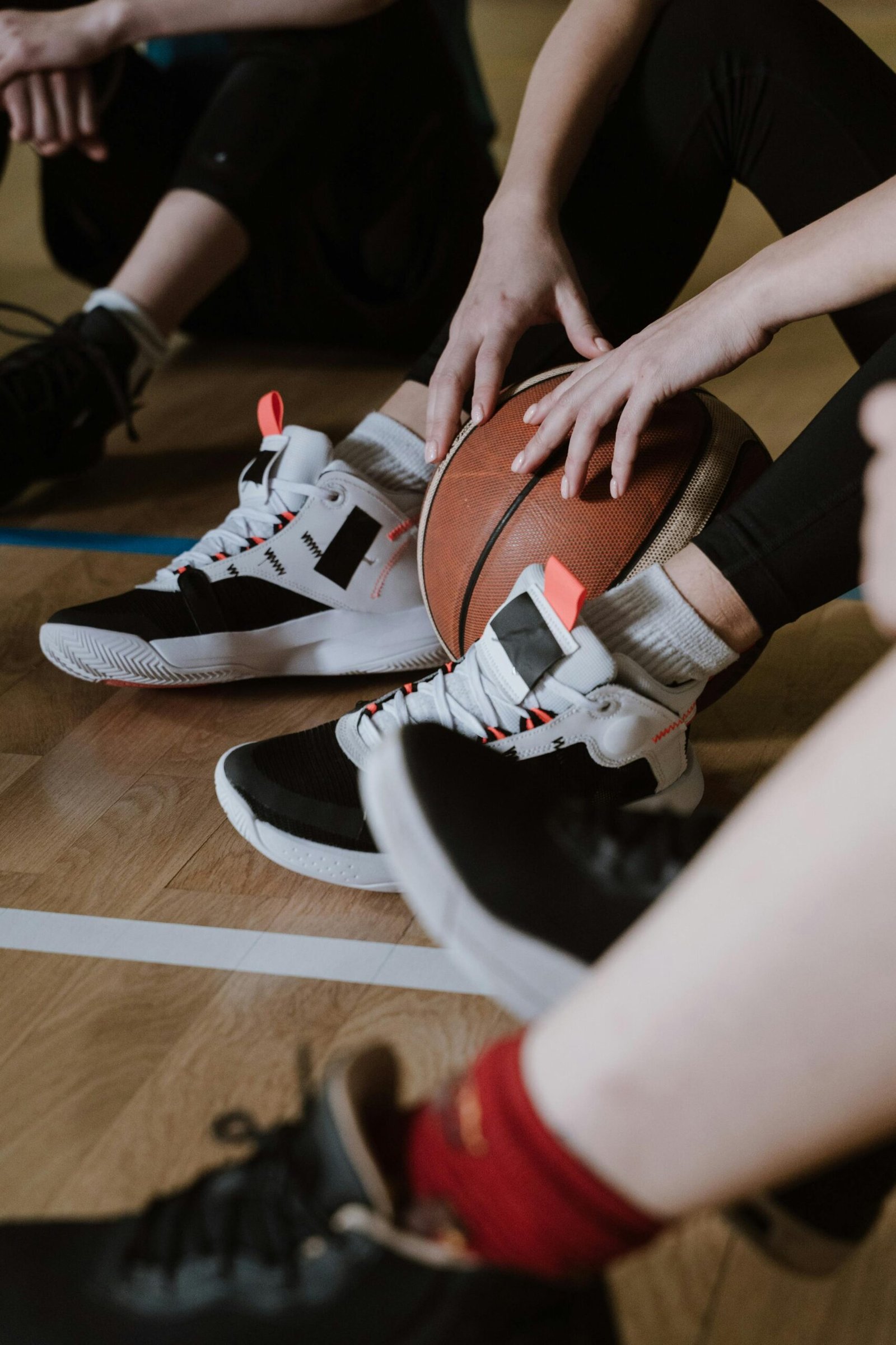 A close-up of athletes resting with a basketball, showcasing sneakers on a wooden court floor.